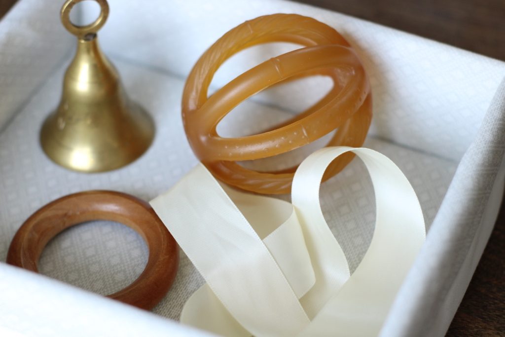 Square basket with a metal bell a ball, a wooden ring and a white ribbon