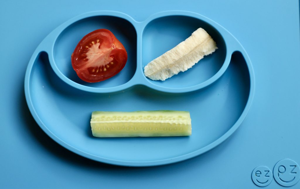 Plate with a quarter of a tomato, a banana spear and a cucumber spear