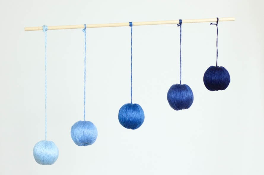 5 spheres wrapped in thread hanging from a wooden dowl as a baby mobile. 