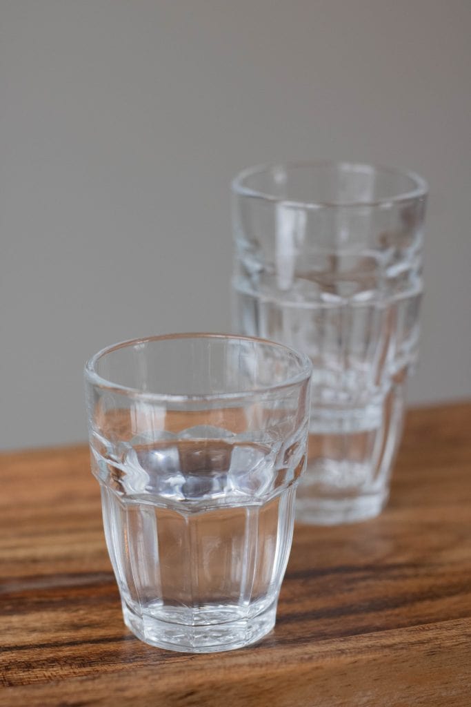 Close up of glass cups. One glass cup has water. Two stacked glass cups in the background. 