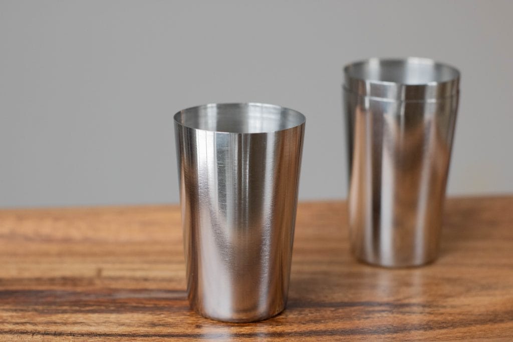Stainless steel shot glass and two stacked stainless steel shot glasses off to the right. 