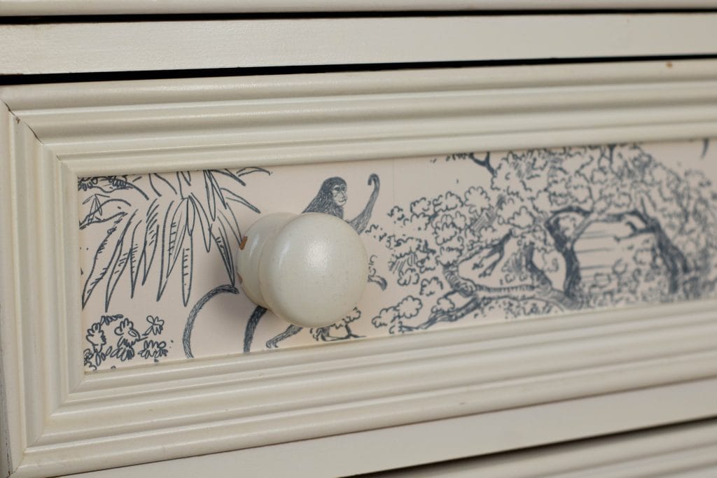 Close up of a dresser drawer with jungle wallpaper and chunky knobs
