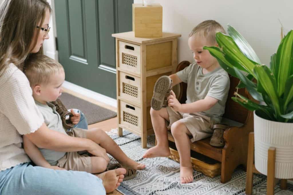 a toddler putting on their shoes on a small bench.