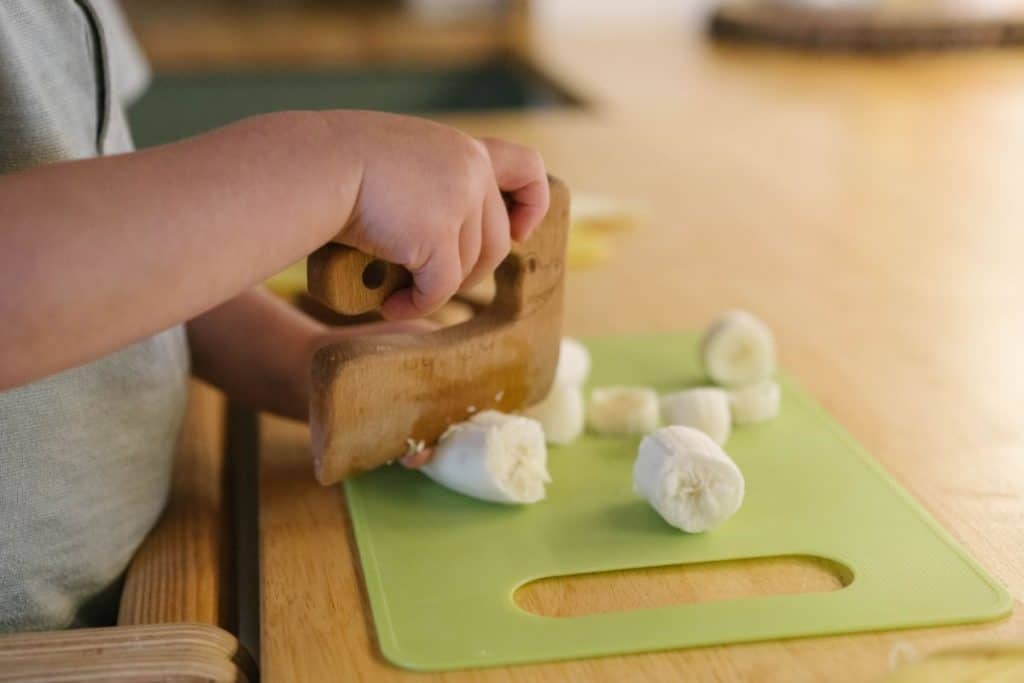 toddler hand slicing a banana with a wooden cutter.