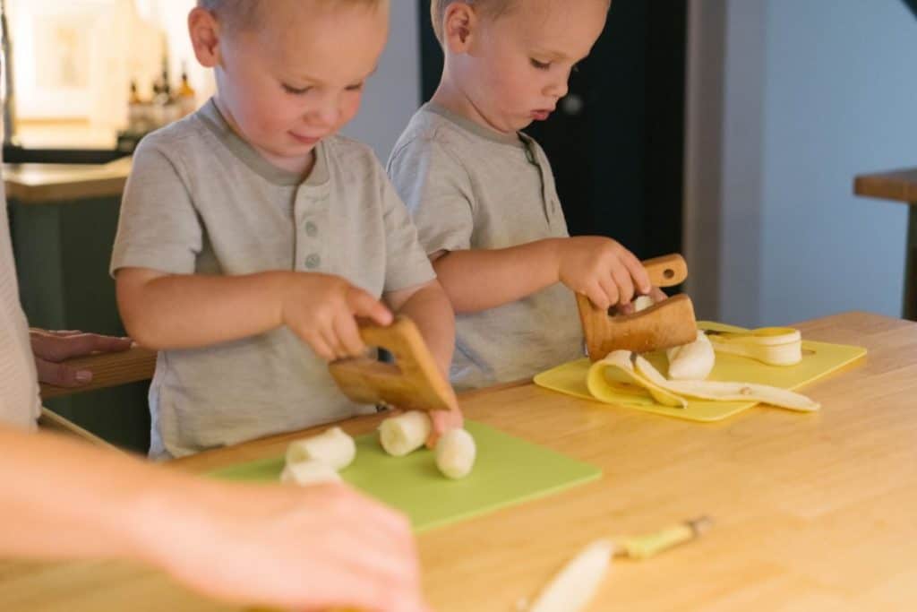 Todlers chopping bananas with wooden chopper.