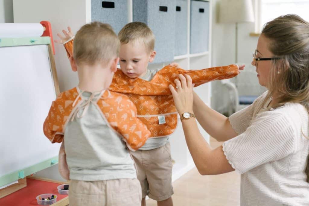 Mom putting on a painting smock onto a toddler.