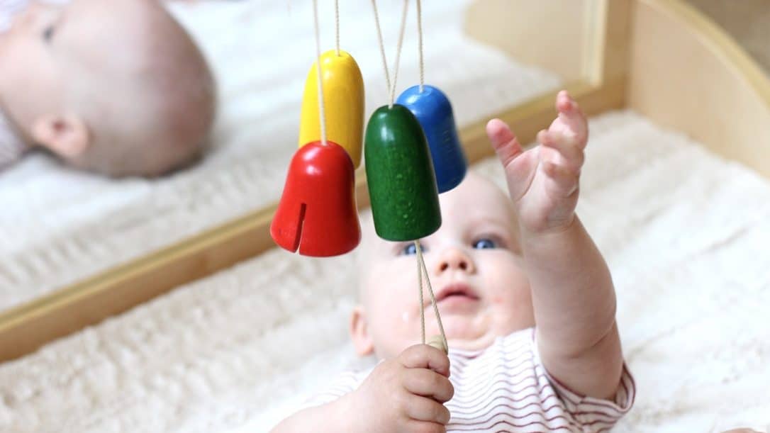 Baby reaching for a wooden bell mobile