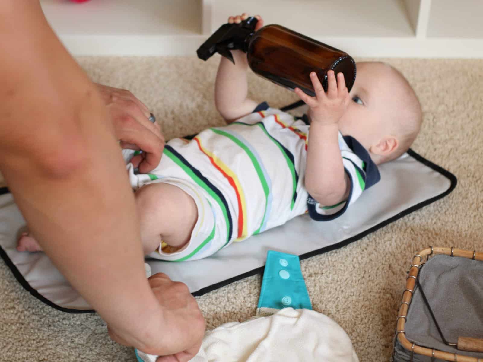 Baby laying on a changing mat holding an amber glass spray bottle