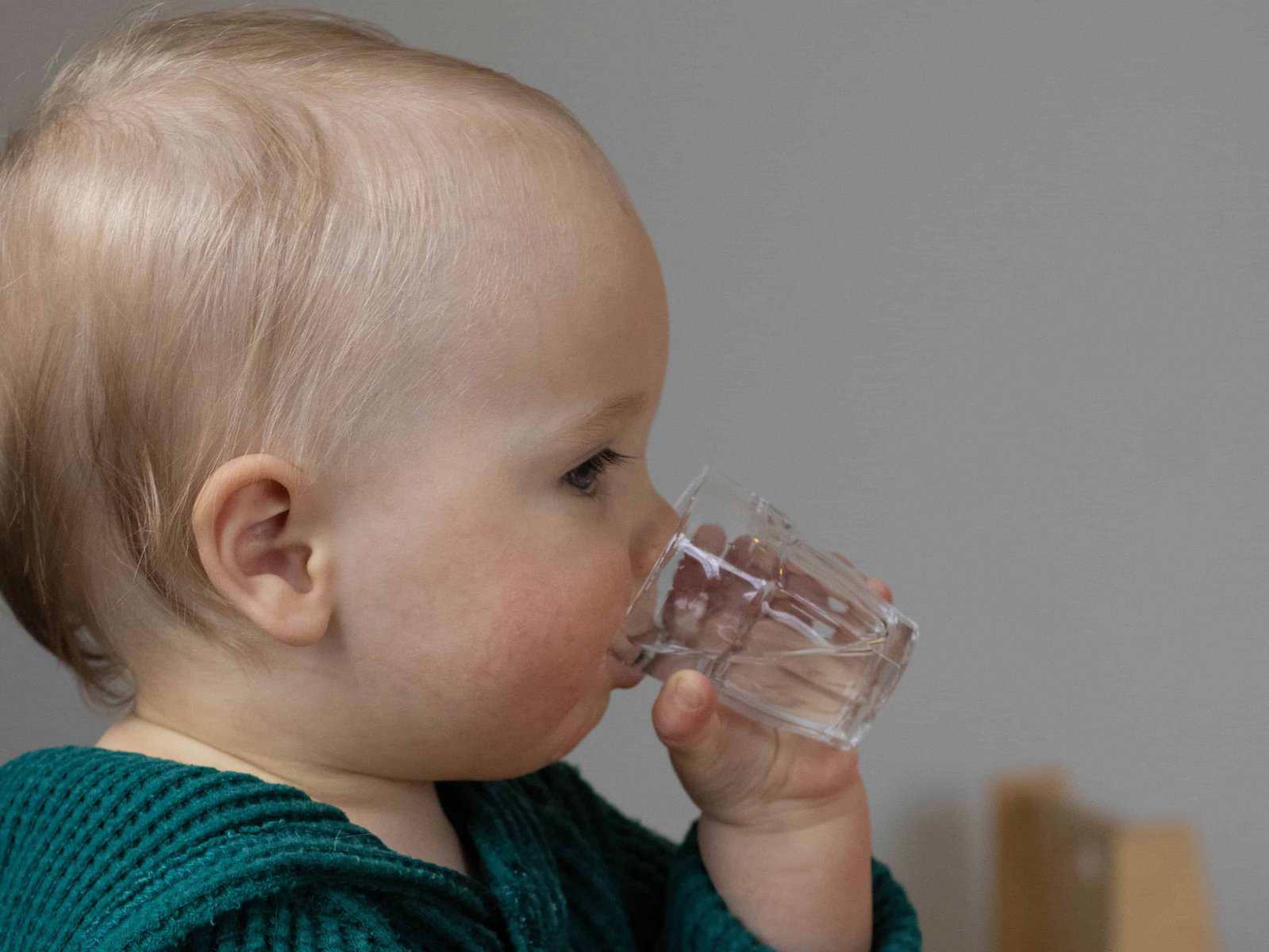 Toddler drinking from an open glass cup