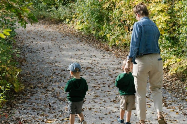 Mom walking with twin toddlers on a walk on a path.