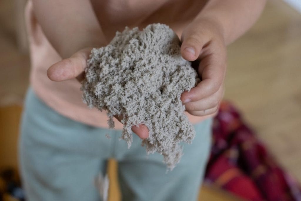 Child holding kinetic sand in hands.