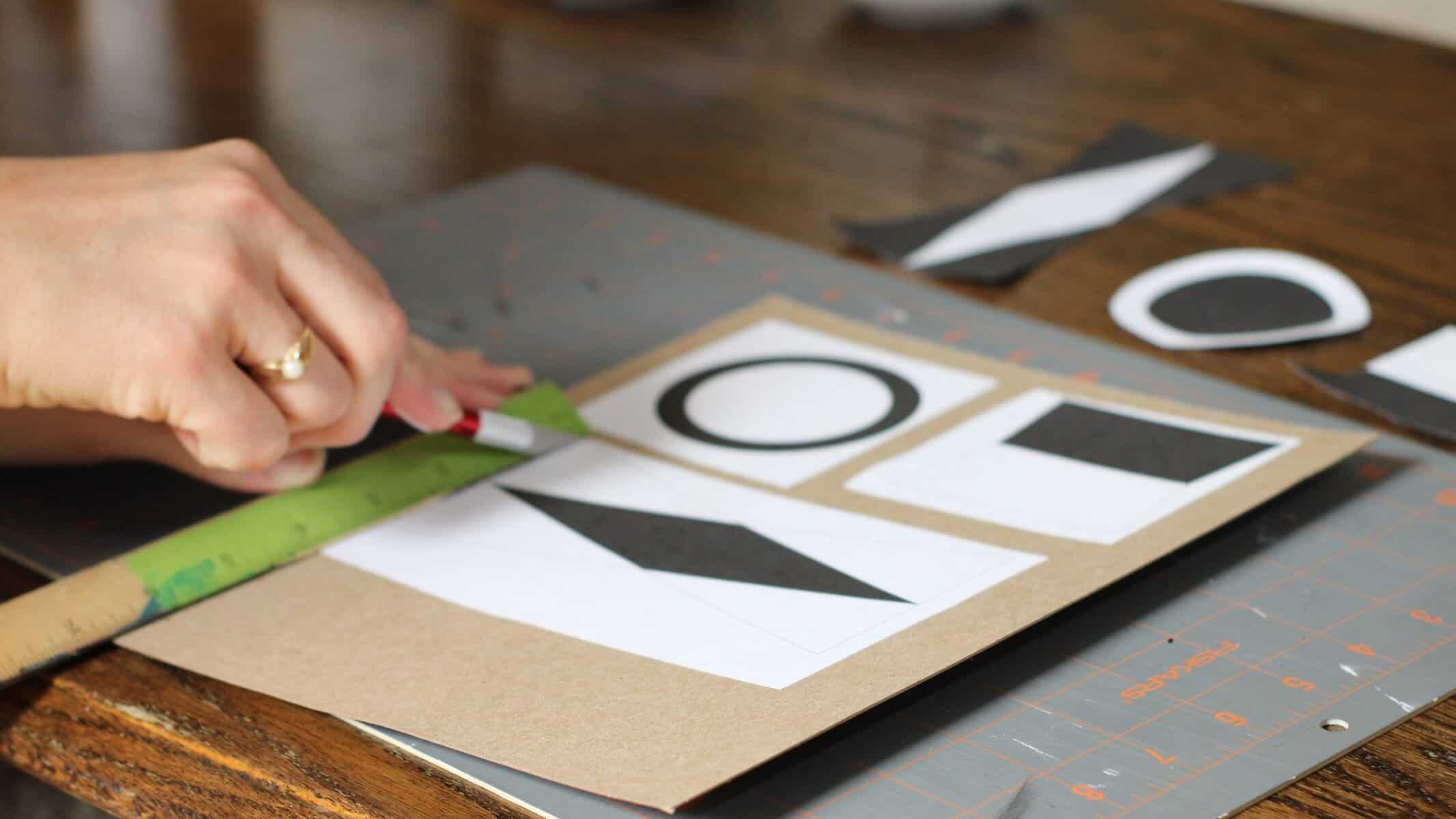 Women's hands using a ruler and an exacto knife to cut out objects for a baby mobile.