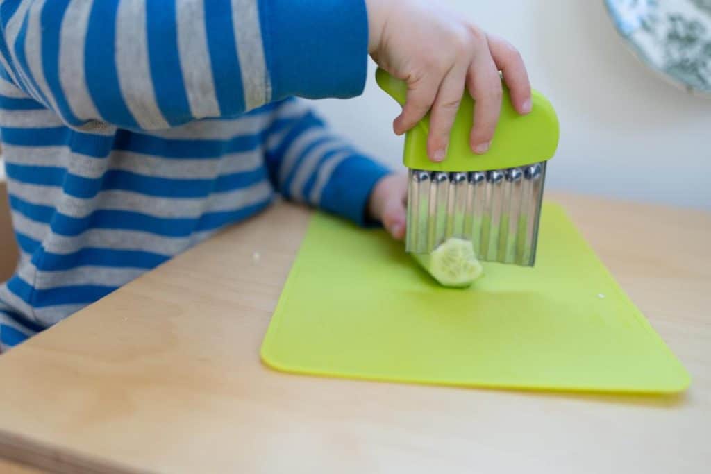 Child chopping a cucumber with a crinkle cutter.