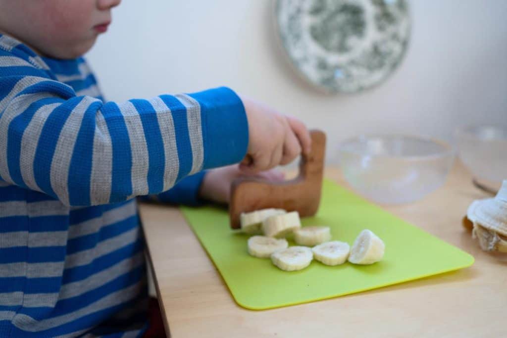 Child chopping a banana with a wooden cutter.