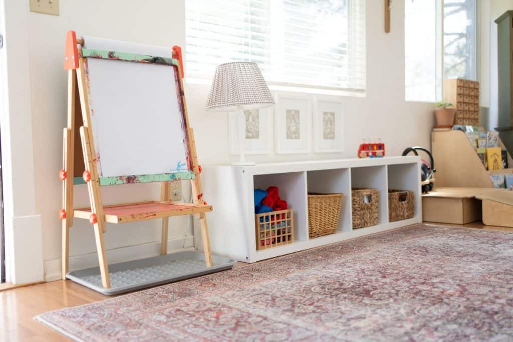 Montessori plalyromm with art easel, shelf with toys and a rug.